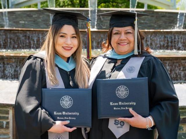 Commencement 2021 - Mom and Daughter - Priscilla and Frezia Valenzuela, standing in front of the Estabrook Garden on campus, wearing their caps and gowns.