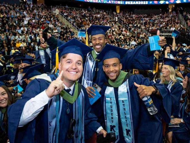 Three young men in blue caps and gowns celebrate at Kean's 2023 commencement.