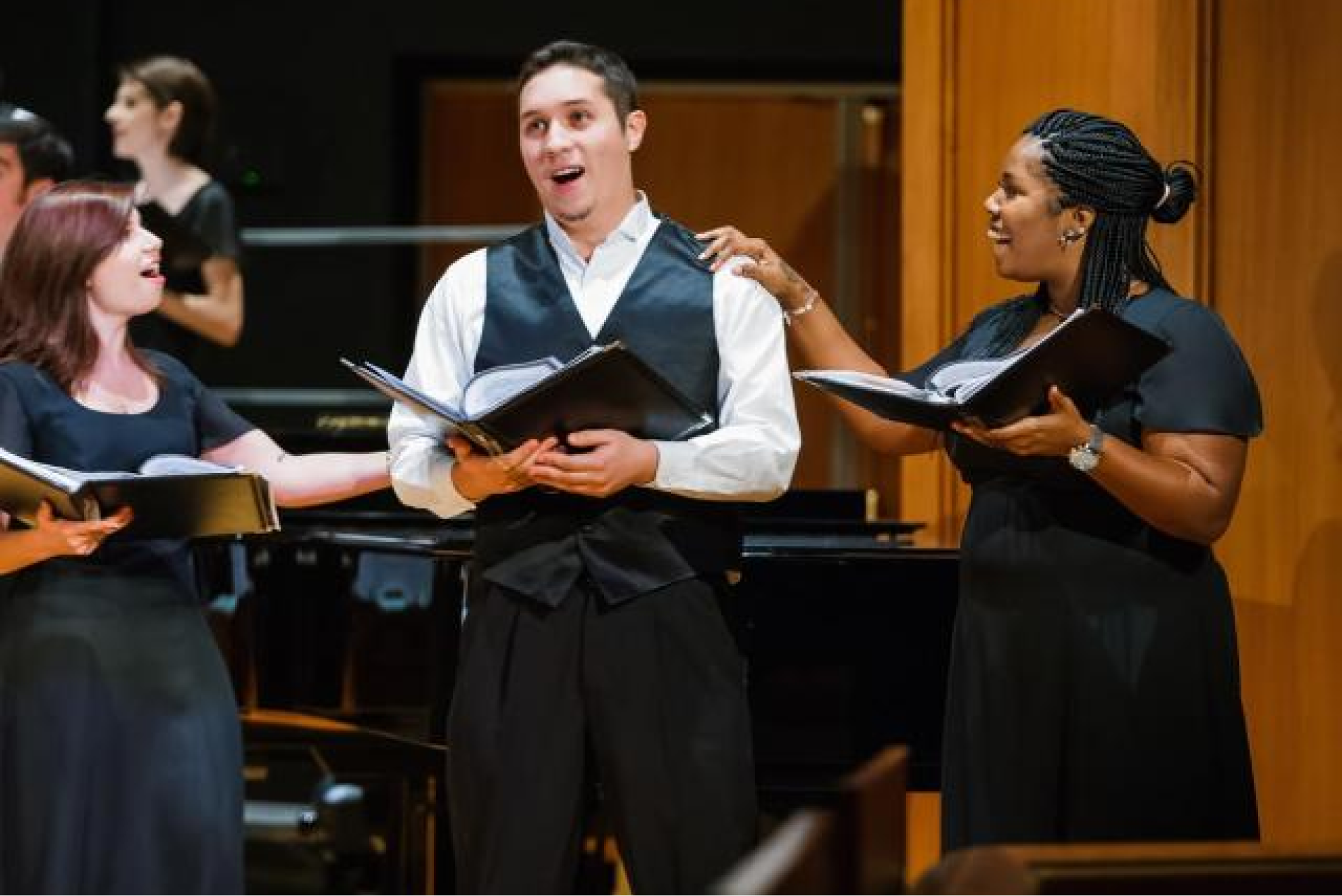 Three student performers singing on stage with open scores