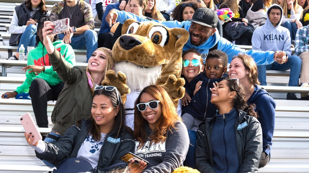 Group of students taking a selfie with Keanu, the Kean mascot, at an outdoor athletics event