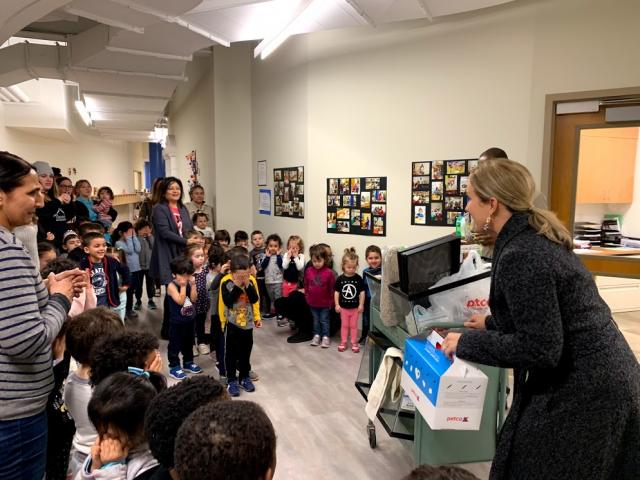 Wolfe holds the hamsters in a box and has a cart next to her with the hamster supplies, as the children look on. 