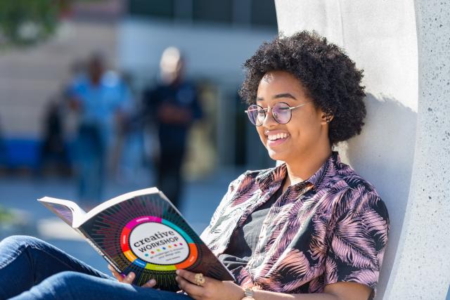 Female student lounging on the MSC patio with a book