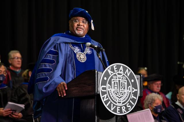 Kean President Lamont Repollet, wearing a cap and gown, speaks at the podium at Prudential Center.