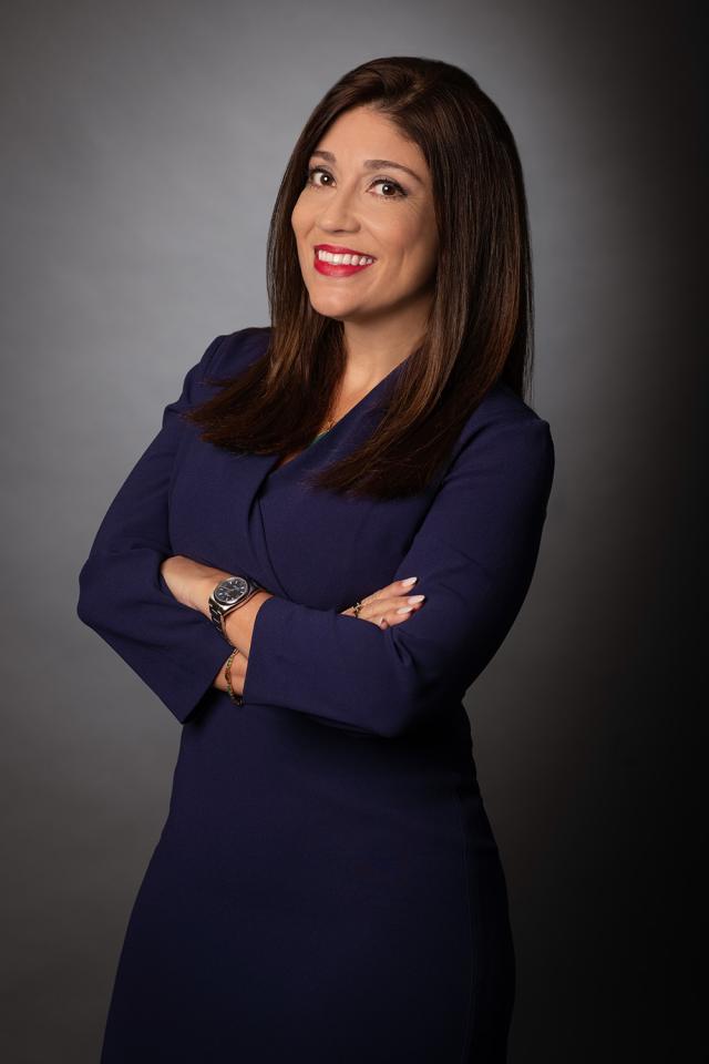 Maria Piastre poses with her arms crossed, wearing a navy blue dress.