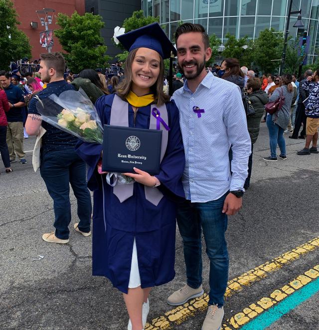 Rachael Johnson in blue cap and gown, holding flowers, stands next to her fiance.