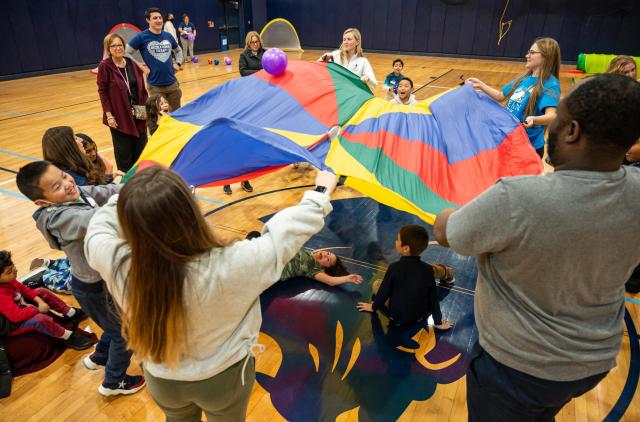 Occupational therapy and recreational therapy students balancing dodgeballs on a rainbow parachute with SONJ children