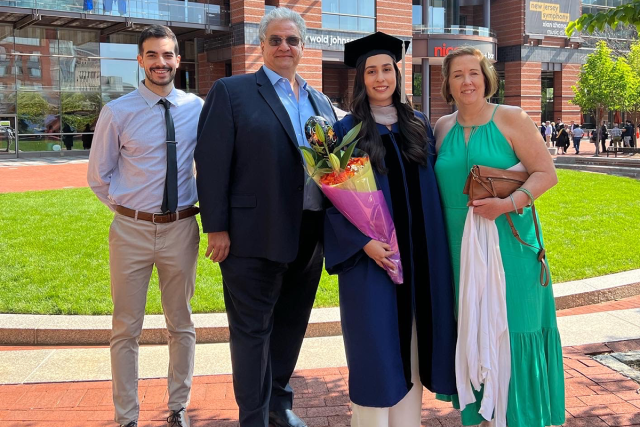 Elizabeth Del Pino, wearing a commencement gown and doctoral tam, poses with her parents and boyfriend.
