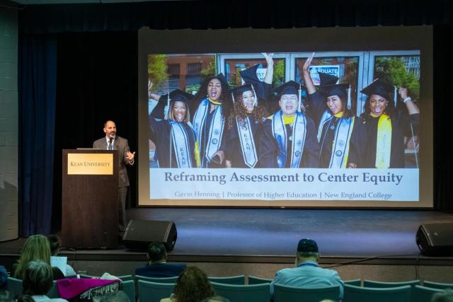 Senior VP Mike Salvatore speaks at a podium in front of a screen reading "Reframing Assessment to Center Equity."