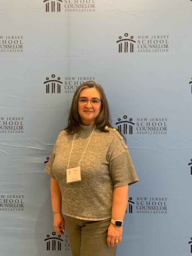 woman standing in front of step and repeat, wearing glasses and a lanyard around her neck