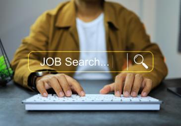 A man's hands on a keyboard. A search bar graphic hovering over them that says 'JOB Search...'