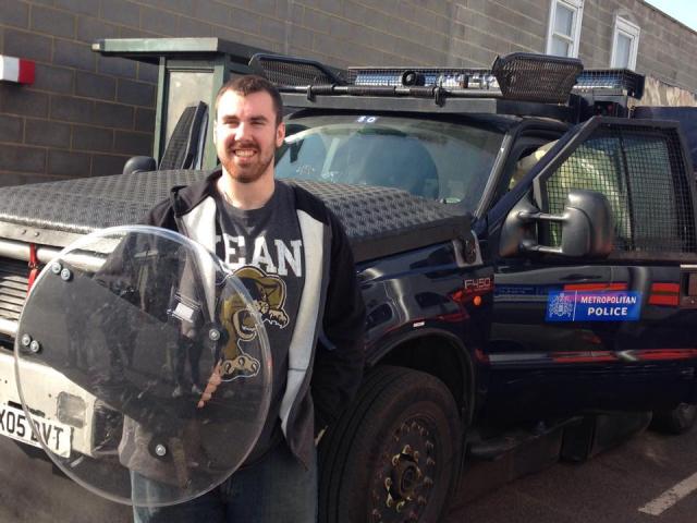 A Kean criminal justice student holds a shield near a Metropolitan Police vehicle.