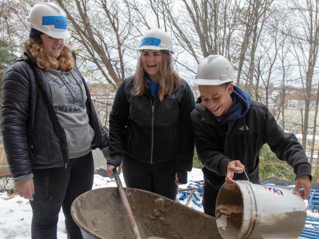 Three students mix the stucco in a wheelbarrow
