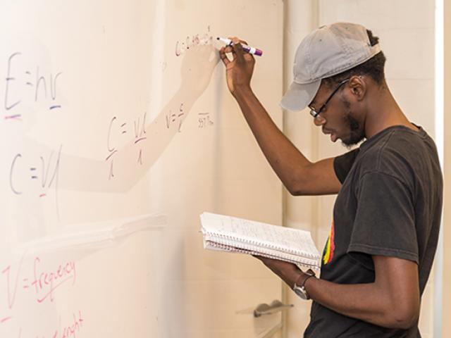 A Kean student works at a whiteboard.