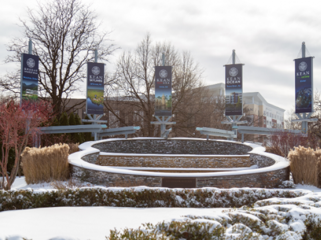 Flags from Kean University's five campuses fly at a fountain on the Union campus in the snow.