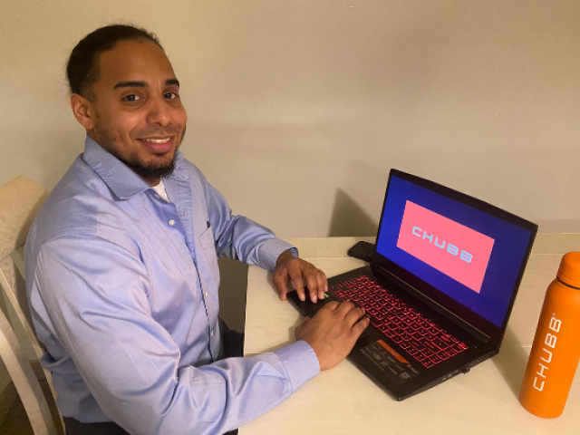 Kean math graduate Angel Rivera sits at a laptop with a Chubb water bottle nearby.