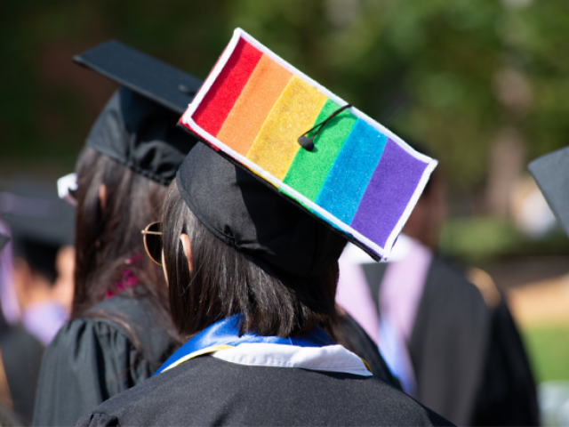 A student wears a graduation cap with the LGBTQIA+ rainbow flag on it at commencement