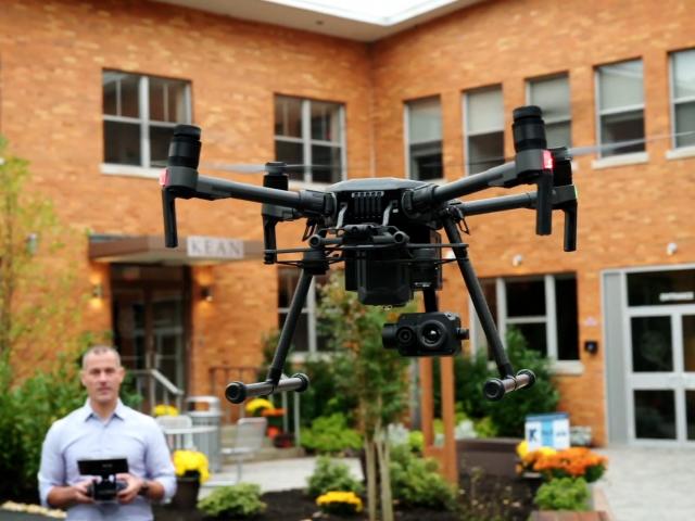 A man operates a drone outside a brick building on the Kean Skylands campus.