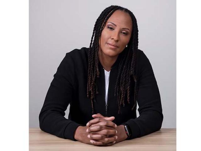 Chamique Holdsclaw, sitting, with her hands folded on a desk.