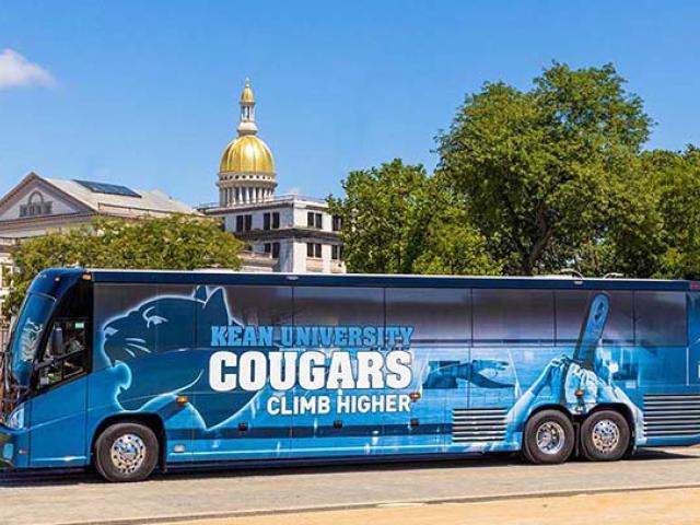 A Kean bus with the words, "Kean Cougars Climb Higher," with the N.J. State Capitol dome in the background.