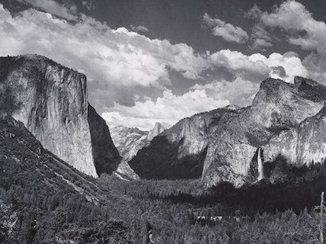 A black and white photo of a landscape of mountains over a sky filled with clouds.