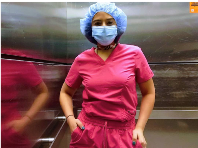 A tan Hispanic woman in bright pink scrubs with a blue mask and blue shower cap. 