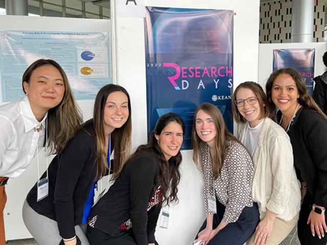 Six young women pose in front of a research poster.