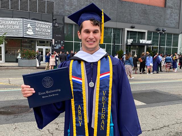 Joseph Fuca, in a blue cap and gown, holds his diploma cover outside the Prudential Center.