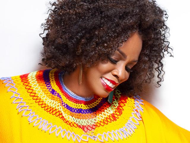 Dianne Reeves in a bright yellow blouse looks down as she smiles.