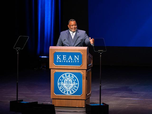 Kean President Repollet gestures as he speaks at a podium onstage at Wilkins Theatre.