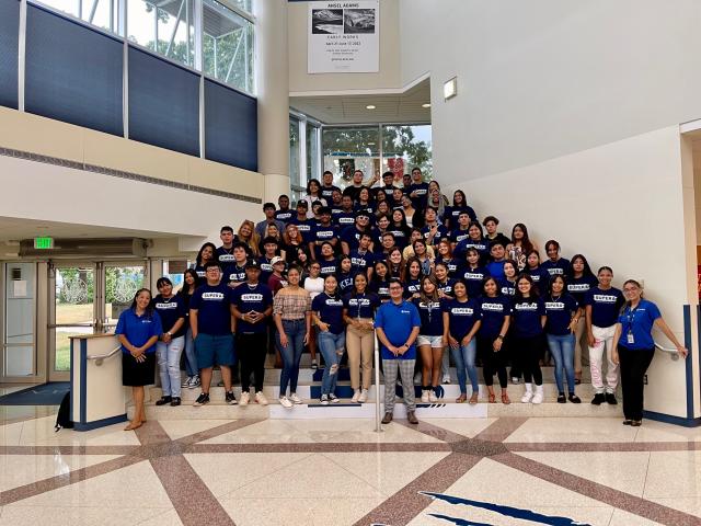 A large group of student wearing blue SUPERA t-shirts pose on a staircase.