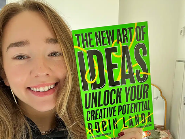 Actor Holly Taylor smiles as she holds up the book, The New Art of Ideas.