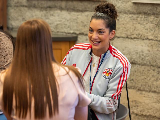 Woman in Red Bulls sweatshirt talks to a student