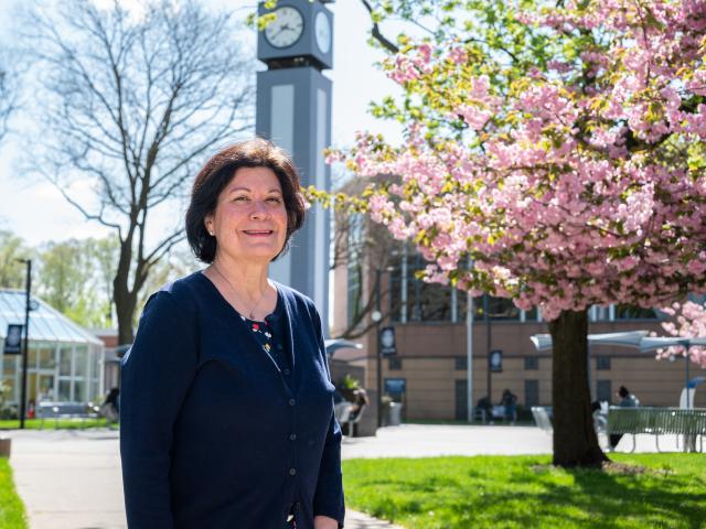 Bernie Moriarty on the Kean campus in front of the clock tower and flowering tree