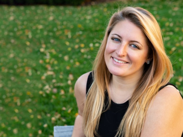 Kelly Bachovchin, a young blond woman, sits on a bench in a grassy area.