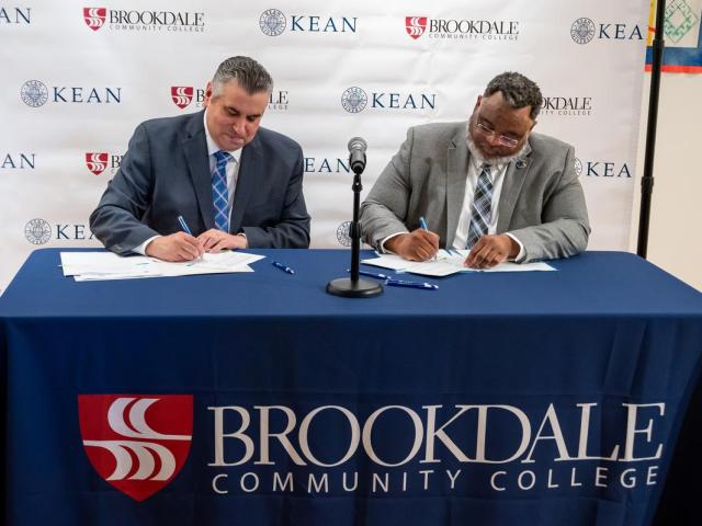 At a desk with a Brookdale sign, President Stout and President Repollet sign documents.