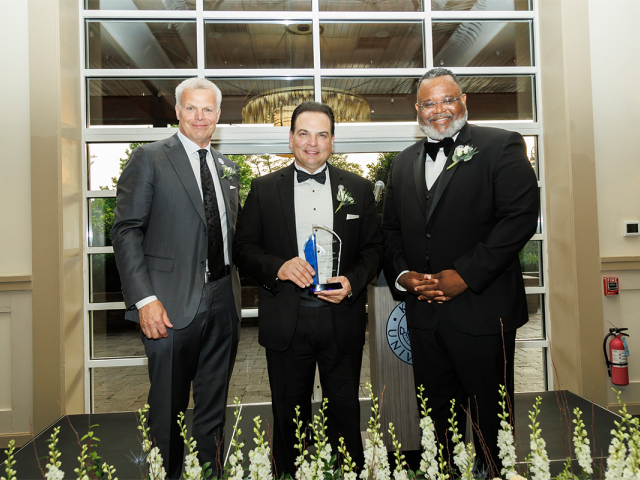 BOT Chair Steve Fastook, Senate President Nicholas Scutari, holding an award, and Kean President Lamont Repollet pose together.