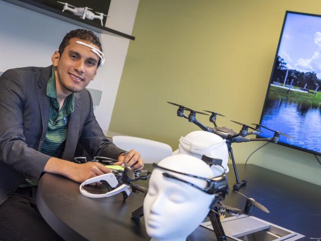 Kean alumnus Marvin Andujar demonstrates a piece of brain interface equipment