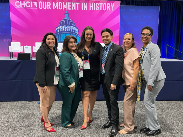 A group of Kean administrators, with a student, pose before a CHCI Our Moment in History sign.