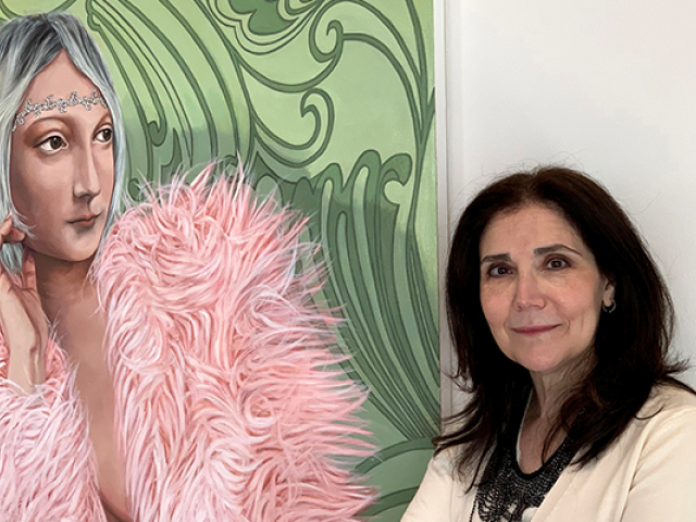 Artist Lisa Ficarelli-Halpern stands before a painting of a woman, with gray hair and pink boa.