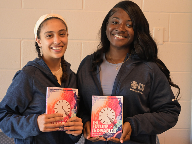 Two female students stand together, holding The Future Is Disabled