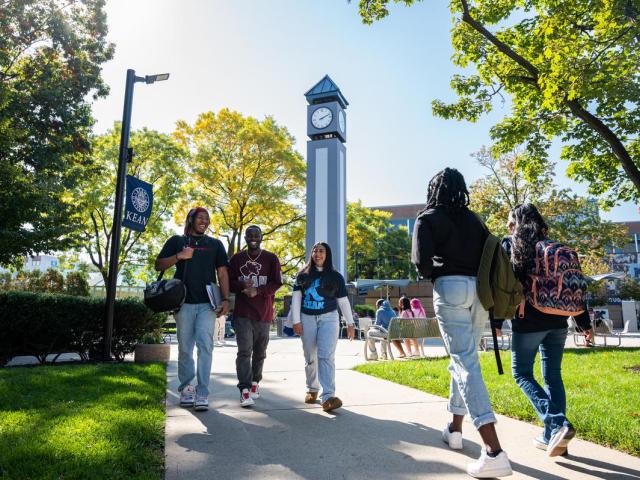 Five students walk on Kean's Union campus, with the blue clock tower in the background.