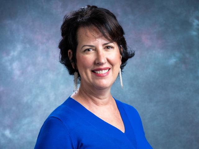 Headshot of a smiling white woman with short dark hair, wearing a blue blouse.