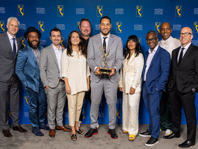 Erik Parker, holding the Emmy Award, stands in the center of a group of people.