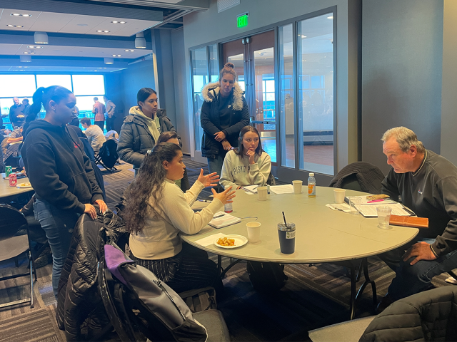 A group of female Kean students in a discussion with a man around a table.