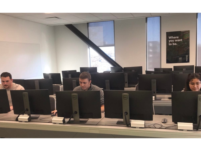 Three students work on separate computer monitors.