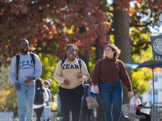Three Kean students in branded sweatshirts walking on campus together on a fall day