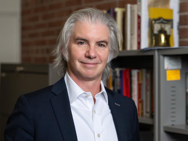 Jonathan Mercantini stands in front of a bookcase and a brick wall