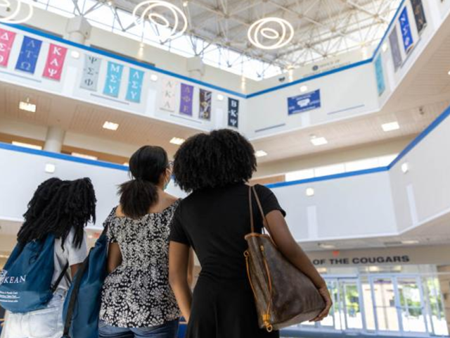 Three young women, one with a Kean backpack, stare up at the ceiling through a skylight.