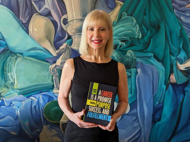 Robin Landa stands in front of a colorful background holding her book