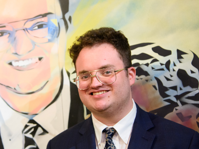 Aidan Allman-Cooper poses in front of his likeness in a mural at Kean